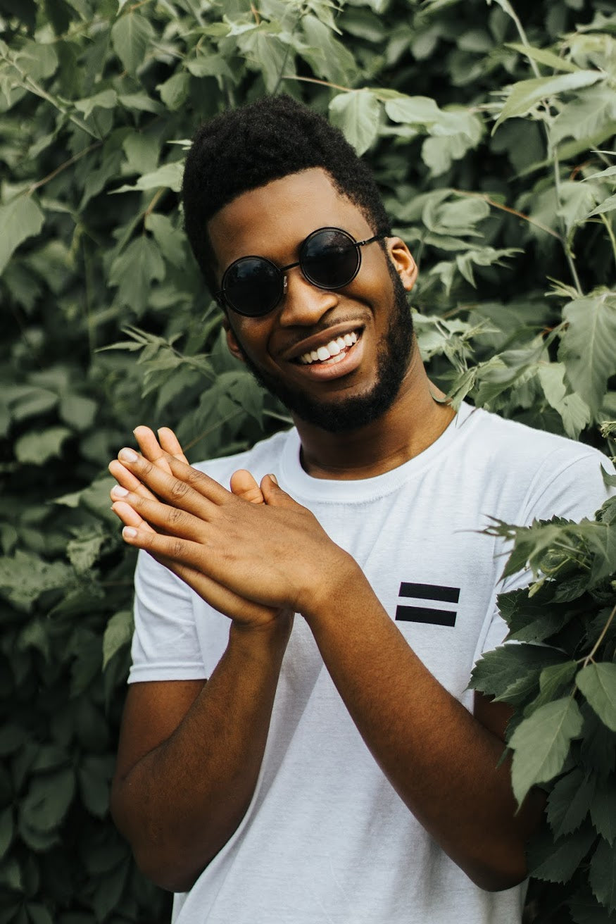 A person smiling at the camera wearing our "No Homophobia" white t-shirt. The shirt has a black equal sign on the left chest. 