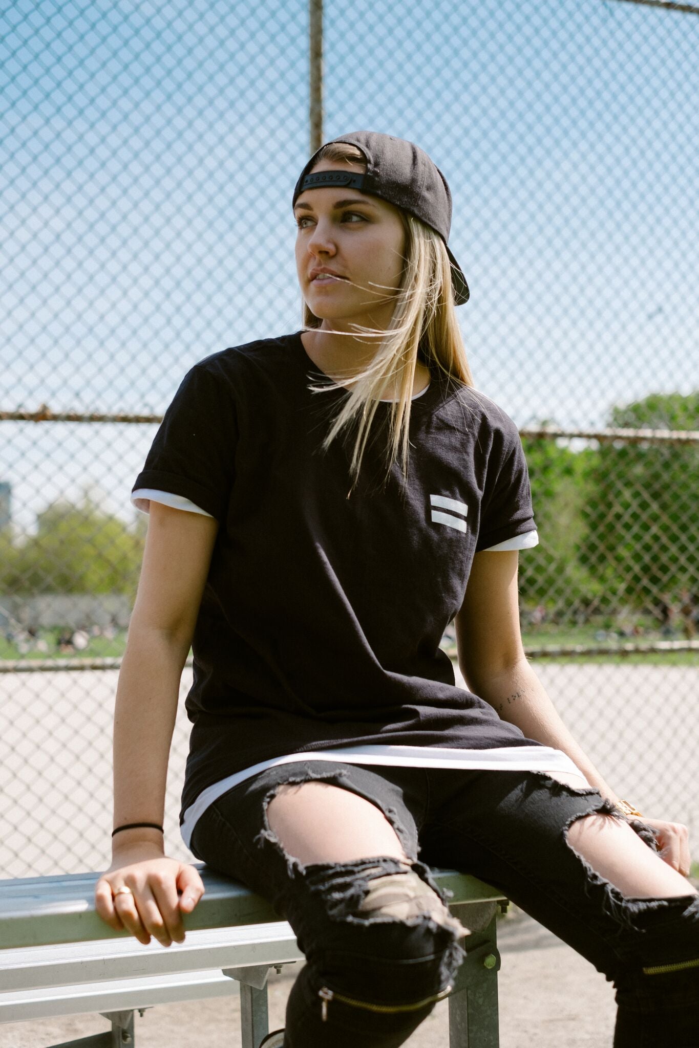 A person sitting on a bench wearing our black No Homophobia t-shirt. The shirt has an equal sign on the lest chest. 